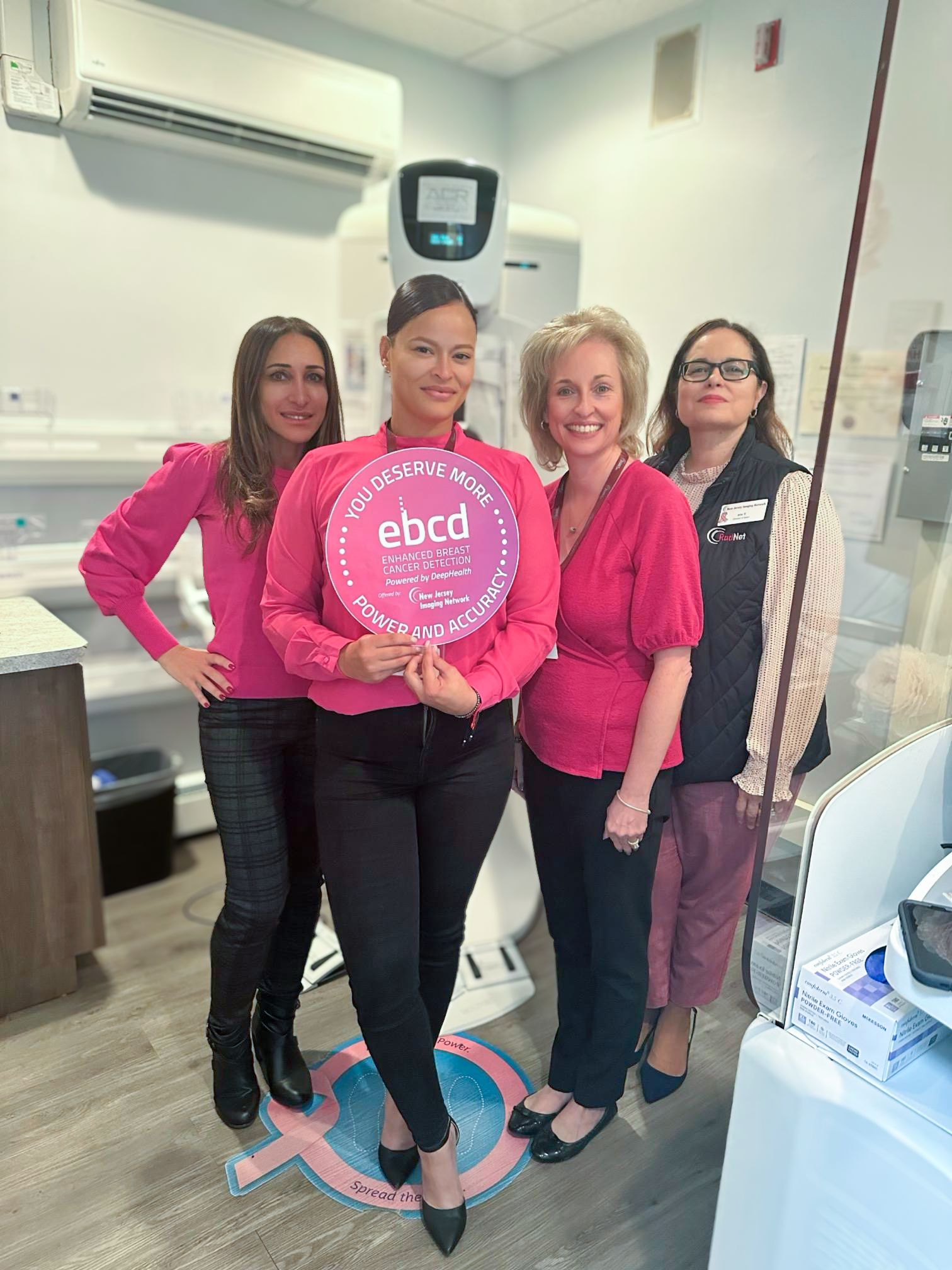 Women at a mammogram unit holding an Enhanced Breast Cancer Detection (EBCD) sign