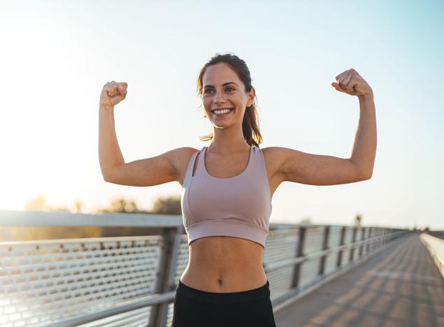 Woman flexing her arms outdoors, celebrating her fitness progress