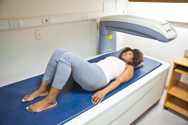 Patient lying on a DEXA scanning table while a technologist prepares the exam